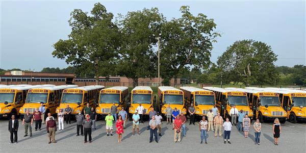 Ariel photo of transportation department standing in front of a row of new, yellow school buses. Ariel photo of transportation department standing in front of a row of new, yellow school buses.
